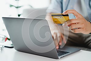 Hand holding credit card and using laptop. Businessman or entrepreneur working from home. Online shopping, e-commerce, internet