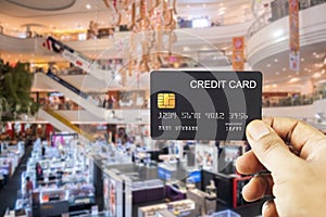 Hand holding credit cards black color with blur defocused supermarket background. shopping purchase and payment concept