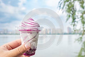 a hand holding a cup of blueberry flavor ice cream on a river side at horizontal composition