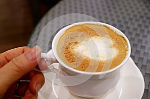 Hand holding a cup of cappuccino coffee with heart shaped latte art