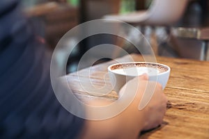 A hand holding a cup of hot coffee with latte art on wooden vintage table