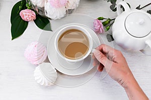 Hand holding a cup of morning coffee and white and pink marshmallow zephyr. Top view, selective focus