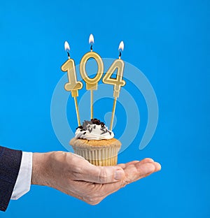 Hand holding a cupcake with the number 104 candle - Birthday on blue background