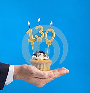 Hand holding a cupcake with the number 130 candle - Birthday on blue background