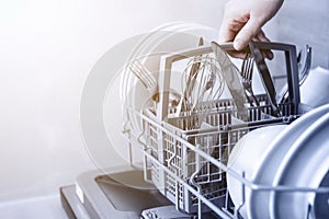 Hand holding cutlery basket with clean cutlery in open dishwasher in kitchen