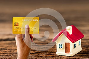 Hand holding demo credit card and house model on wood background.