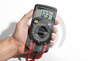 Hand holding a digital multimeter displaying 12.3 volts on a white background {Ai generated