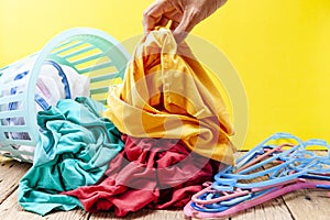 Hand holding dirty laundry in washing basket on wooden plank,yellow background