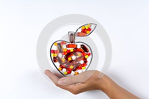 Hand holding drawing apple with colorful capsules and pills on white background. Health care vitamins or synthetic food concept.