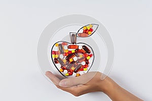 Hand holding drawing apple with colorful capsules and pills on white background. Health care vitamins or synthetic food concept.