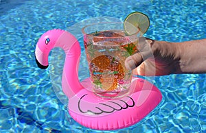 Hand holding a drink in an inflatable pink flamingo drinks holder in swimming pool