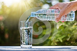 Hand holding drinking water bottle pouring water into glass on wooden table