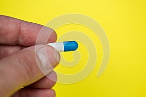 Hand holding drugs pills capsule on yellow background