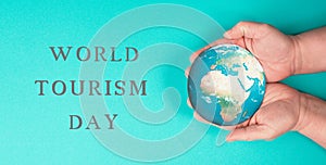 Hand holding the earth globe, world tourism day is standing next to it, trip around the world, travel concep