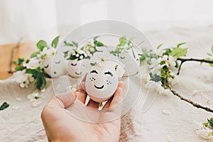 Hand holding easter egg with drawn sleeping face in floral wreath on soft rustic background