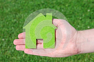 Hand holding eco house icon concept on the green grass background