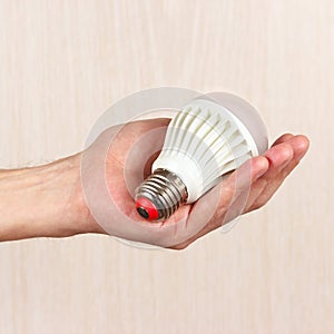 Hand holding ecofriendly led lightbulb on light wood background