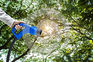 Hand holding Electric car charger. Electric Vehicle EV Charging station on blurred nature with soft light background.  Air polluti