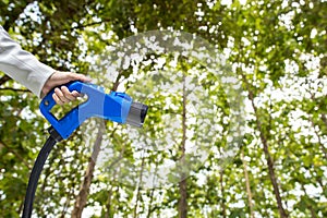 Hand holding Electric car charger. Electric Vehicle EV Charging station on blurred nature with soft light background.  Air polluti