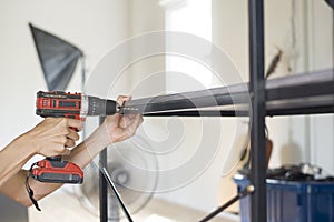 Hand holding an electric drill is drilling steel furniture table.