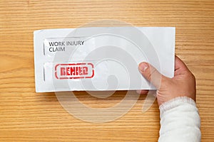 Hand holding an envelope with work injury claim application inside stamped with denied stamped