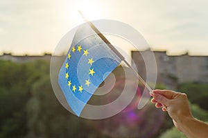 Hand holding European Union flag in an open window. Background blue sky, silhouette of the city, sunset