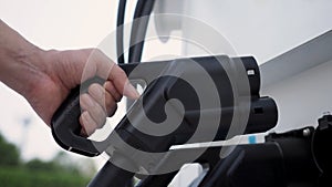 Hand holding EV charging plug in front of camera with blurred background