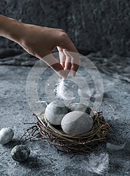 Hand holding feather over nest with Easter eggs on blue background. Happy Easter holiday