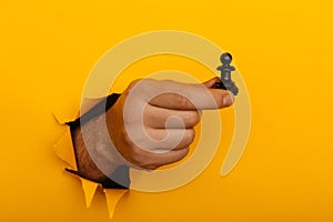 Hand is holding figure of pawn through a hole of yellow background