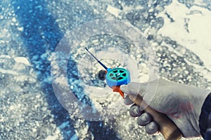 Hand holding fishing rod lowered into hole in winter