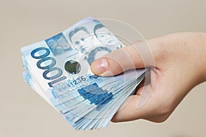 Hand holding folded bundle of blue money in cash of one thousand Philippines peso. Giving bribe, paying bills or getting salary. P