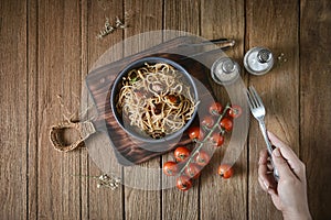 Hand holding the fork with Italian spaghetti pasta, mussel, tomato and garnish on round dish and wooden plate