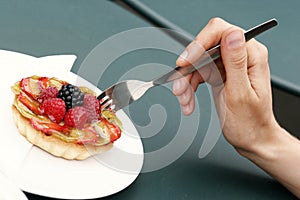 A hand holding a fork poking a fruit pie. Conceptual image shot