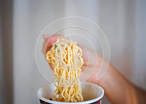 Hand holding fork to eat spicy instant noodles in cup