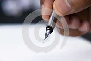 A hand holding fountain pen in air and blue Ink dripping out of the nib having white paper below