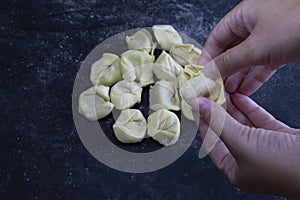 Hand holding fresh Ravioli on floury dark background. Italian homemade healthy food concept