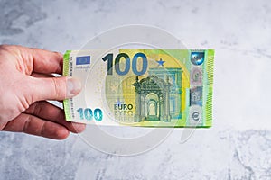 Hand holding and giving one hundred 100 euro banknotes. Money in man hands on gray background