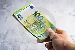 Hand holding and giving one hundred euro banknotes. Stack of money in man hands on gray background