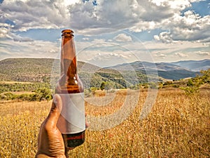 Hand holding a glass beer beverage outdoors, Sierra Madre del Sur mountains in the background. Travel in Mexico