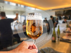 Hand holding a glass of frothy beer in a restaurant