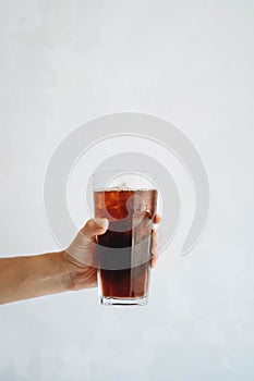 Hand holding a glass of homemade cold brew coffee on white table
