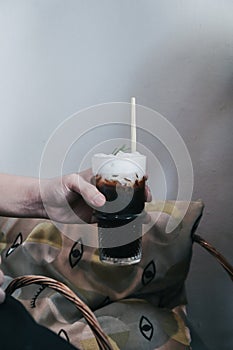 Hand holding a glass of iced black coffee with milk foam on top vintage background