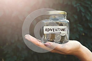 Hand holding glass jar with coins for adventure