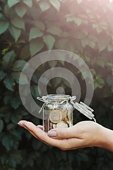 Hand holding glass jar with coins, green backdrop