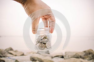 Hand holding glass jar contain with coin at the beach