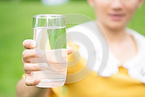 Hand holding glass of pure water on green nature background, healthy concept