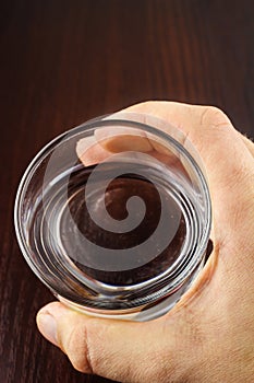 Hand holding glass of purified water on wooden table, top view