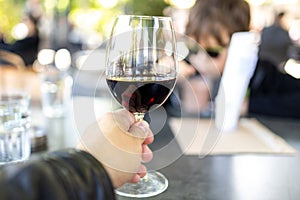 Hand holding a glass of red wine on a table in a restaurant.