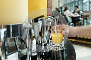 Hand holding glass refill orange juice for row of fresh juice at