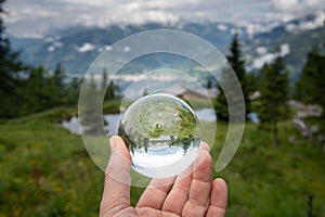 Hand holding glass sphere in front of pasture in the alps